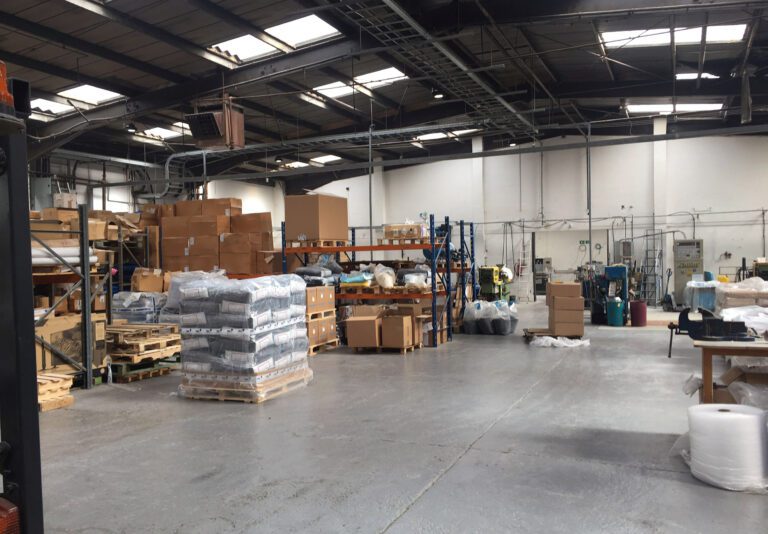 Organized warehouse interior with shelves full of cardboard boxes, pallets, and scattered equipmen