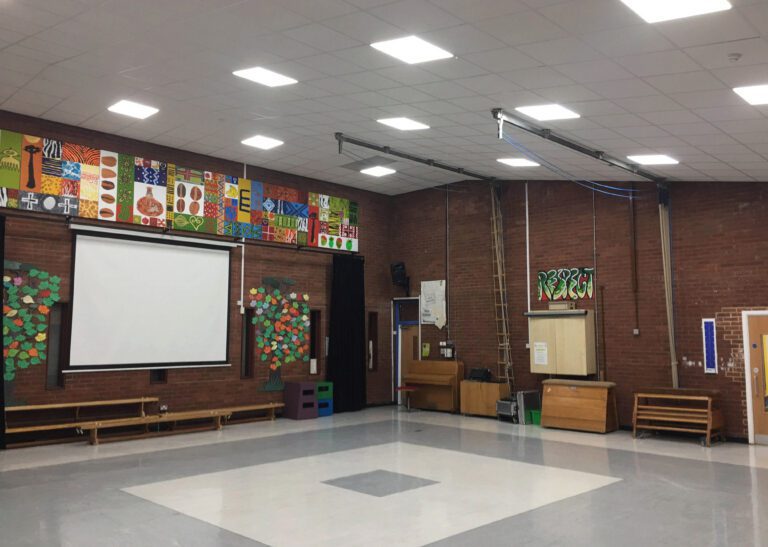School gym with high ceiling, colorful mural 'THEATRE,' paper trees, and projection screen