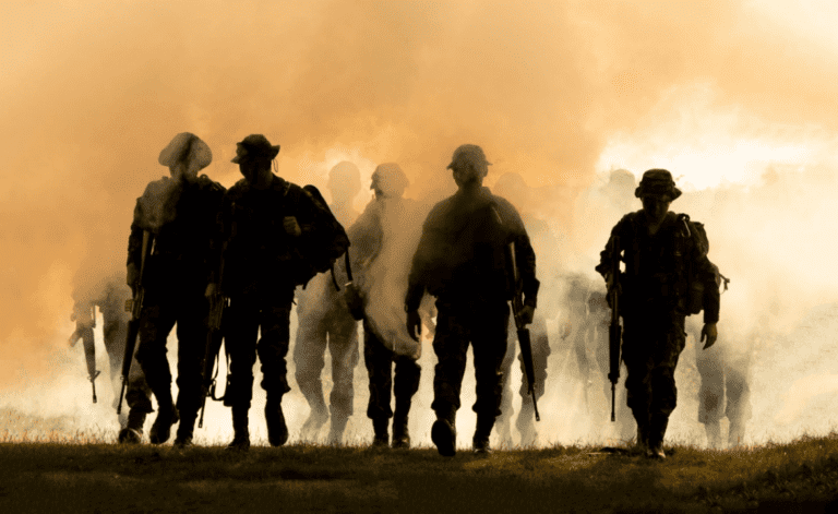 The image showcases a smoky battlefield where silhouetted soldiers advance through an orange-tinted haze, carrying rifles and clad in military gear.
