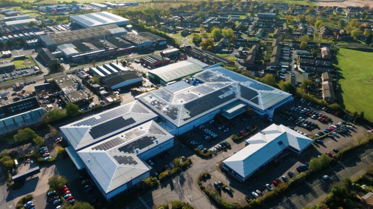 Aerial view of industrial buildings with solar-paneled roofs, surrounded by parking lots and greenery.