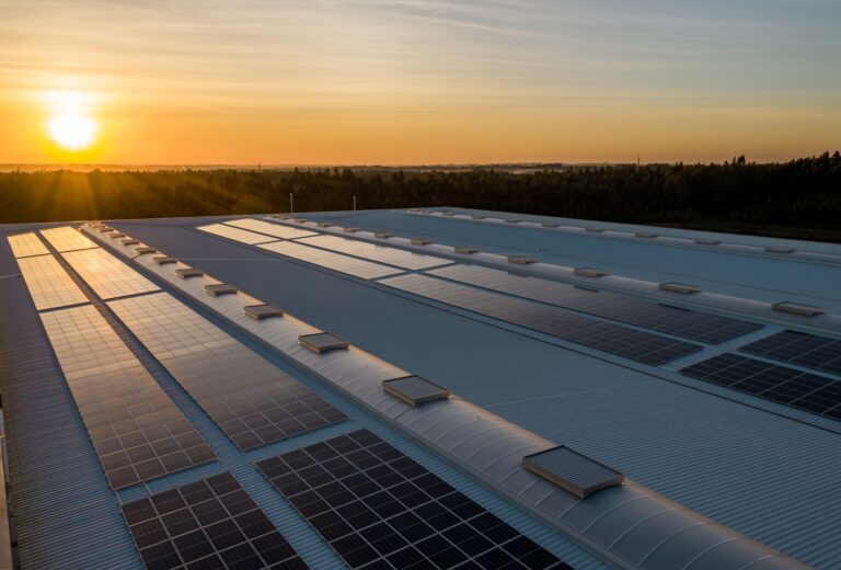 An array of solar panels on top of a commercial building at sunset.