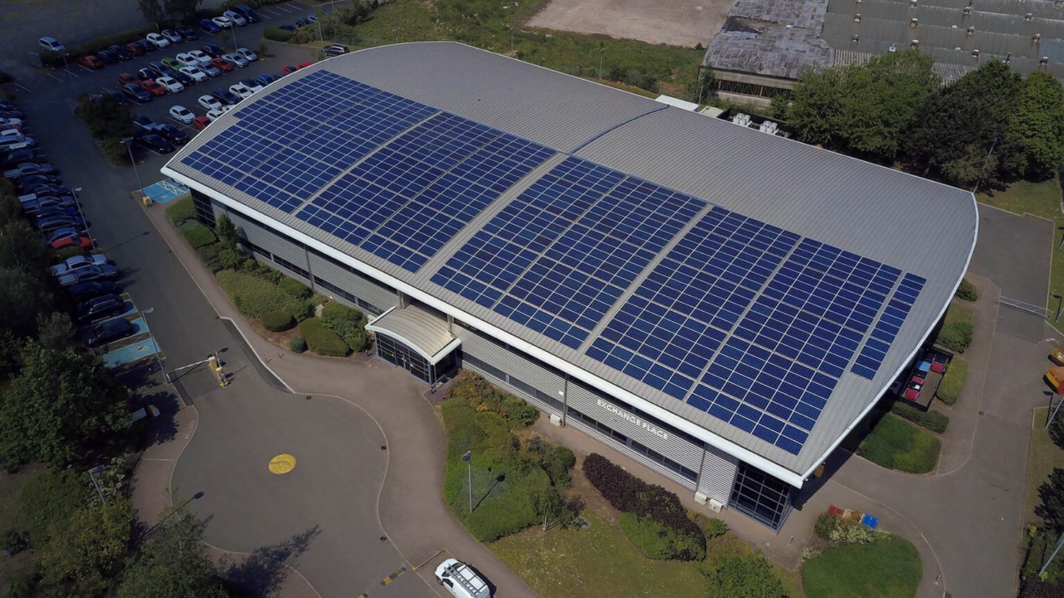 Aerial view of Exchange Place building with solar panels on its curved roof, surrounded by parking and greenery.