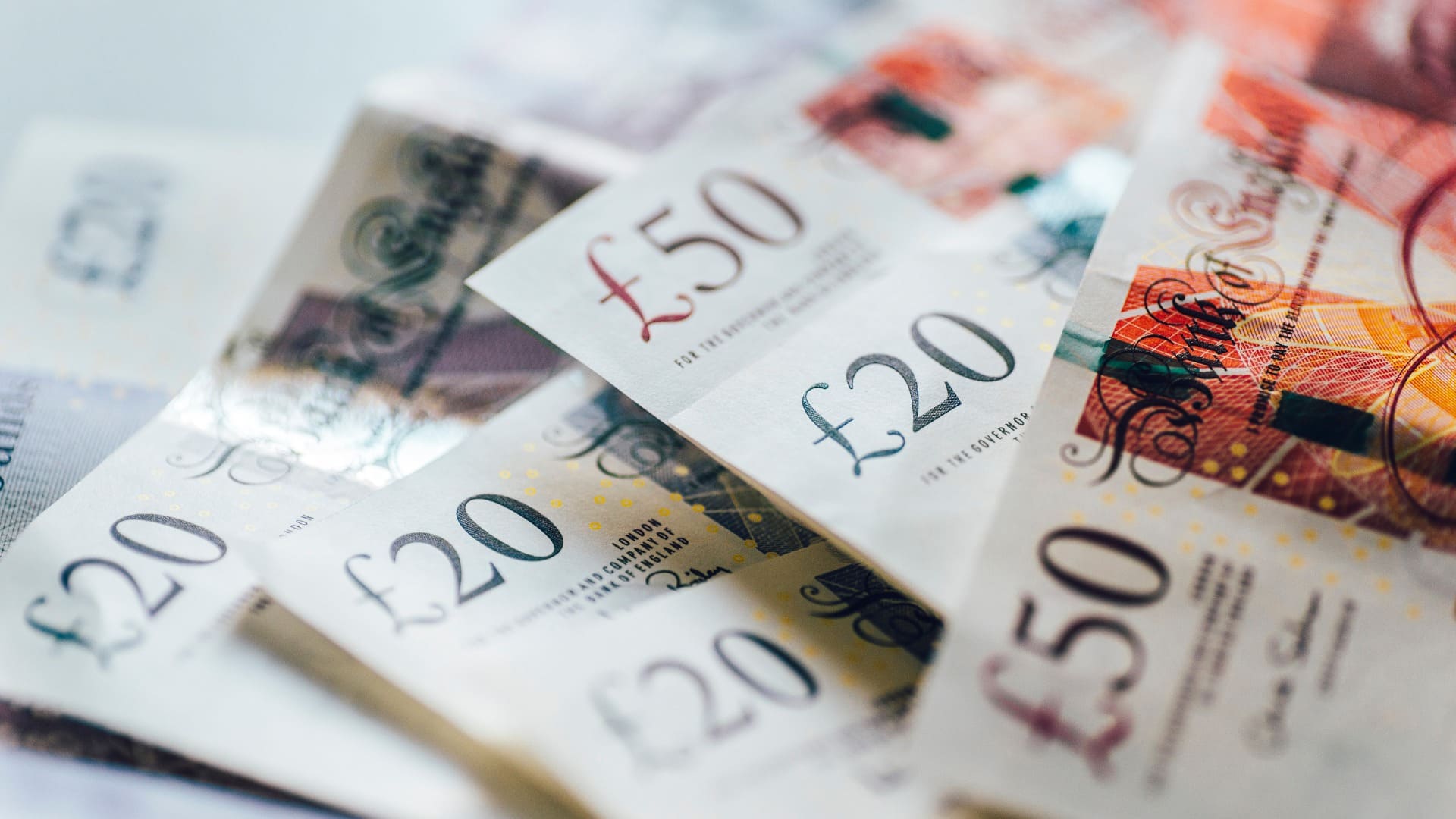 Spread of overlapping British pound banknotes, featuring denominations of £20 and £50, essential for transactions.