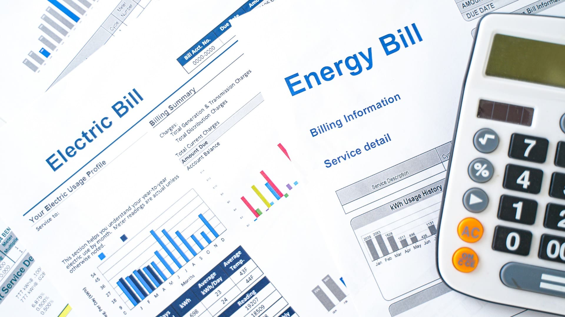 Documents about electric bills, charts, graphs, and a calculator on a table for energy analysis.