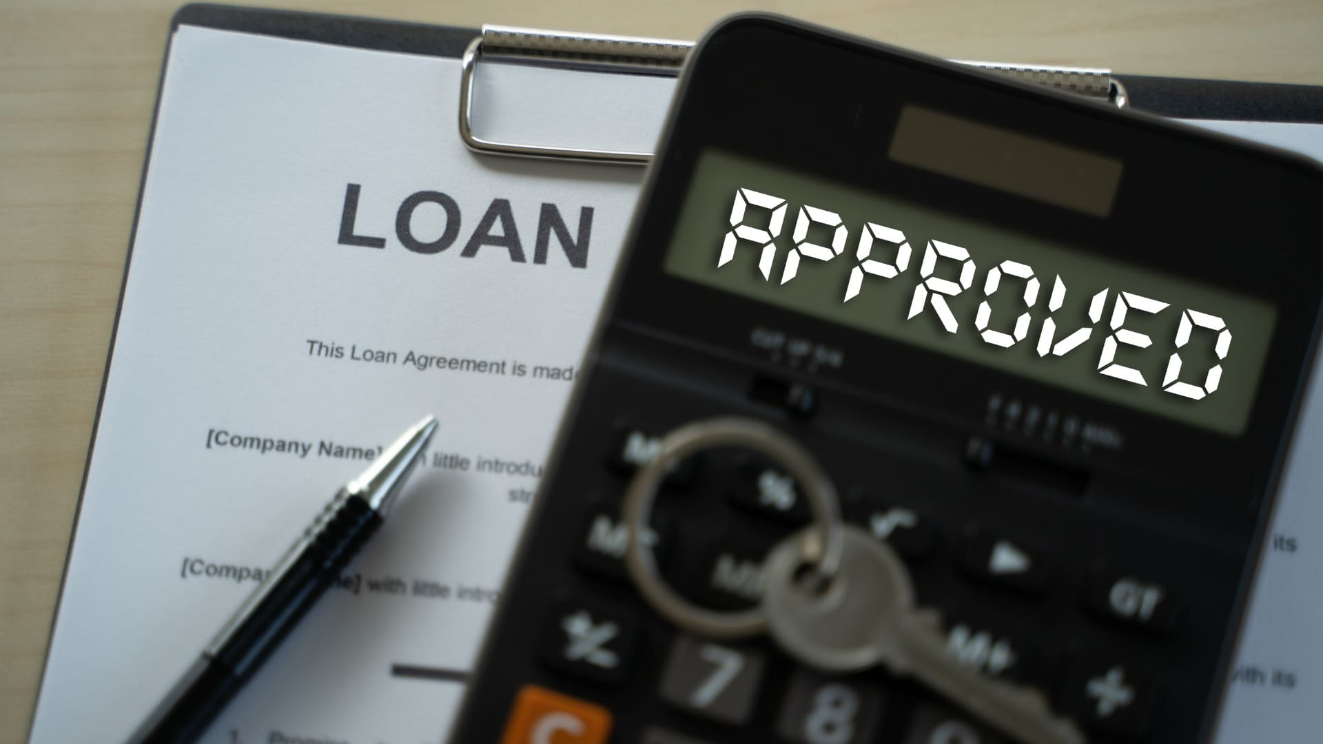 Loan document, keys, pen, and a calculator displaying 'APPROVED', symbolizing successful loan approval.