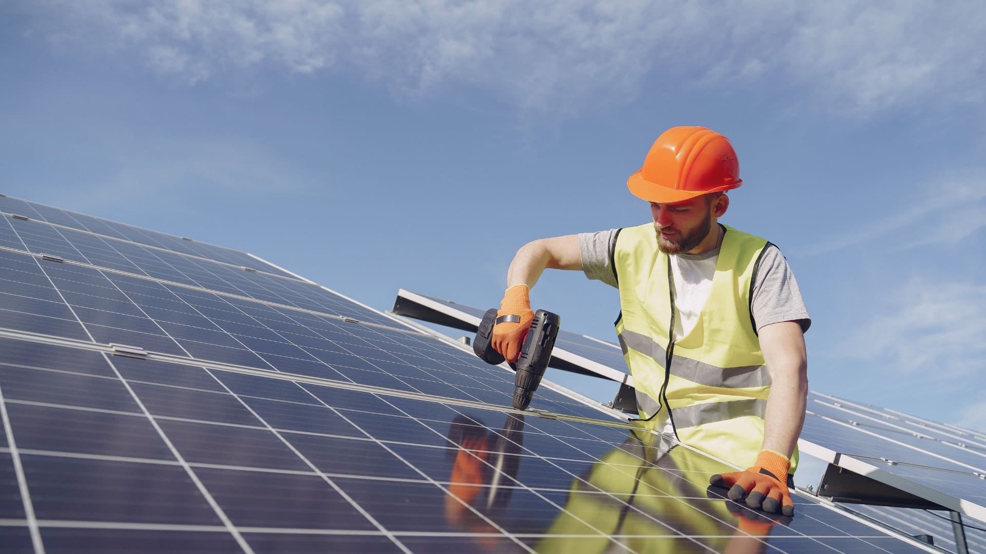 Worker kneeling on solar panels under bright sunlight.