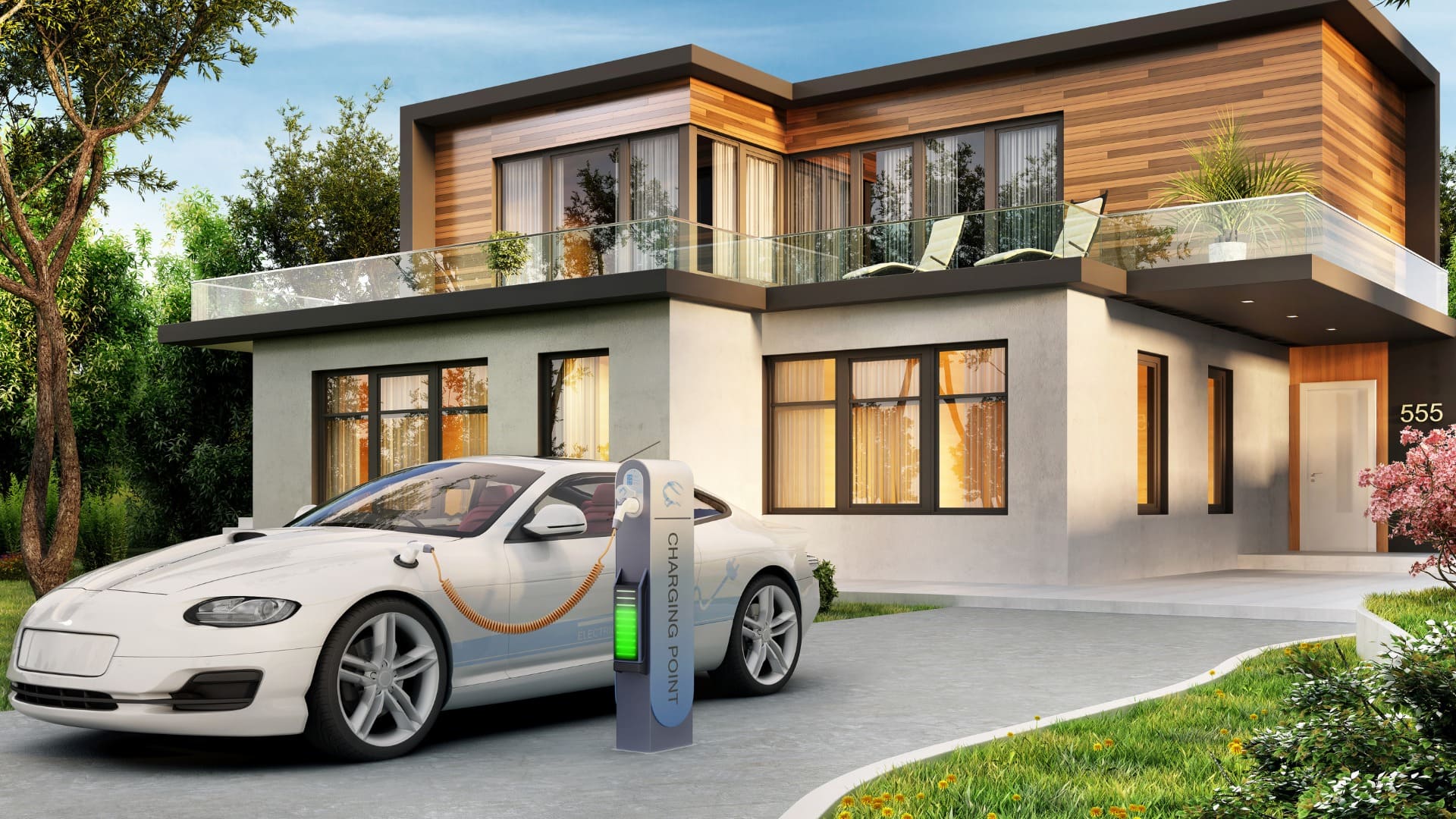 A modern two-story house featuring a mix of wood and concrete materials on its exterior, with a flat roof and large windows. The upper floor boasts a balcony with glass railings, furnished with outdoor furniture for relaxation. A white electric car is parked on the driveway, connected to a charging station labeled 'CHARGING POINT,' which is illuminated with a green light, indicating an active charge. The house number '555' is displayed near the entrance, surrounded by a landscaped yard with bushes, trees, and vibrant flowers.