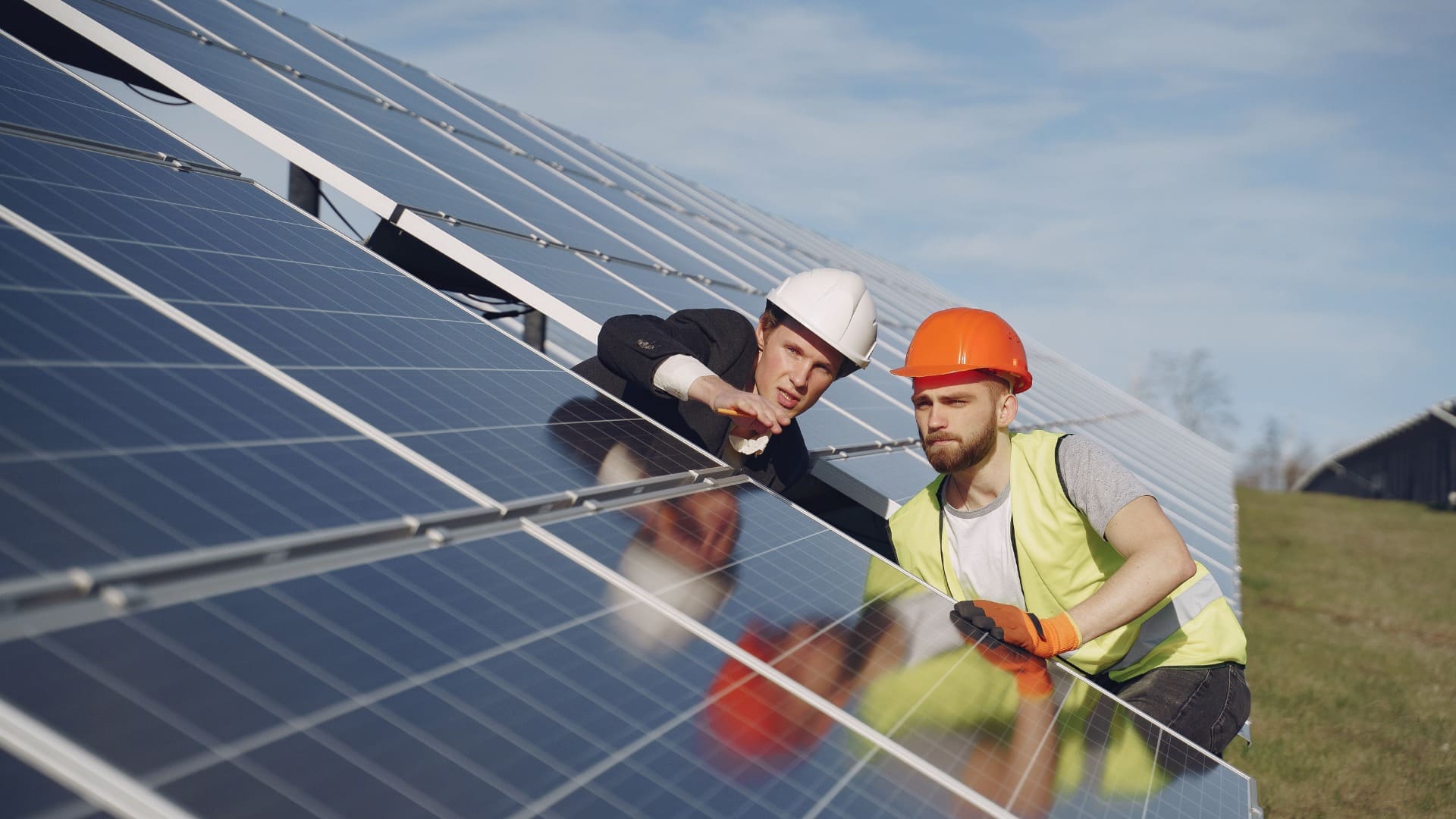 Two workers installing solar panels in a grassy area, emphasizing renewable energy solutions.