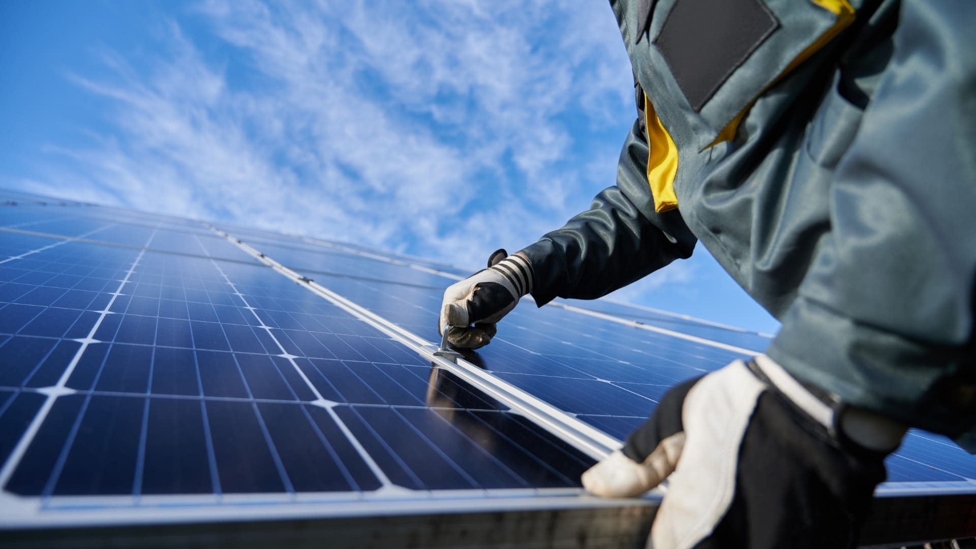 Worker adjusting solar panel under sunny sky, highlighting renewable energy installation process.