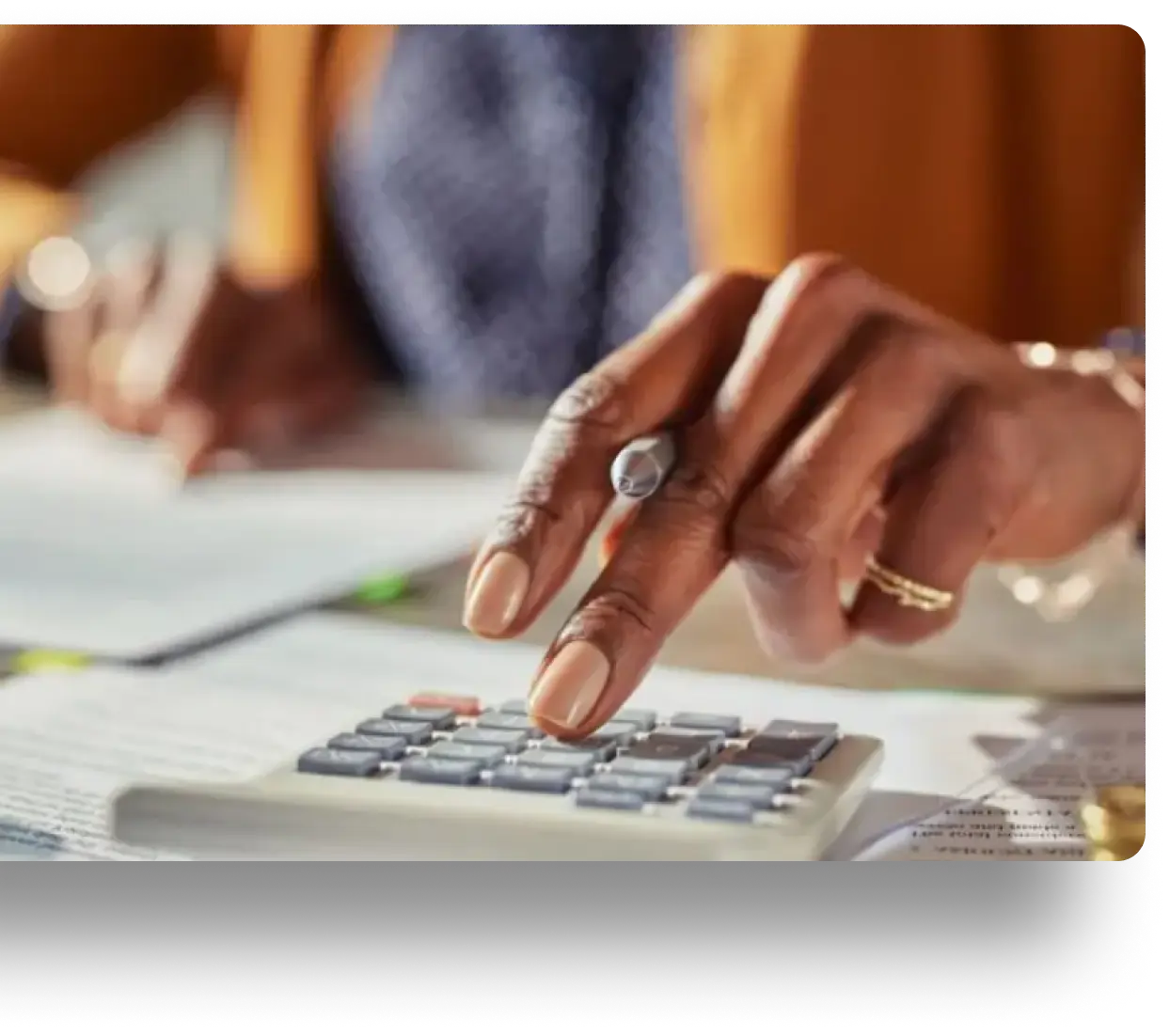 Hand pressing buttons on a calculator amidst papers and documents in soft focus.