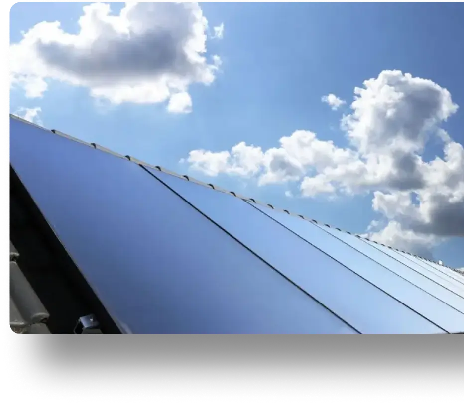 Section of solar panels on a rooftop reflecting the blue sky and scattered clouds above.