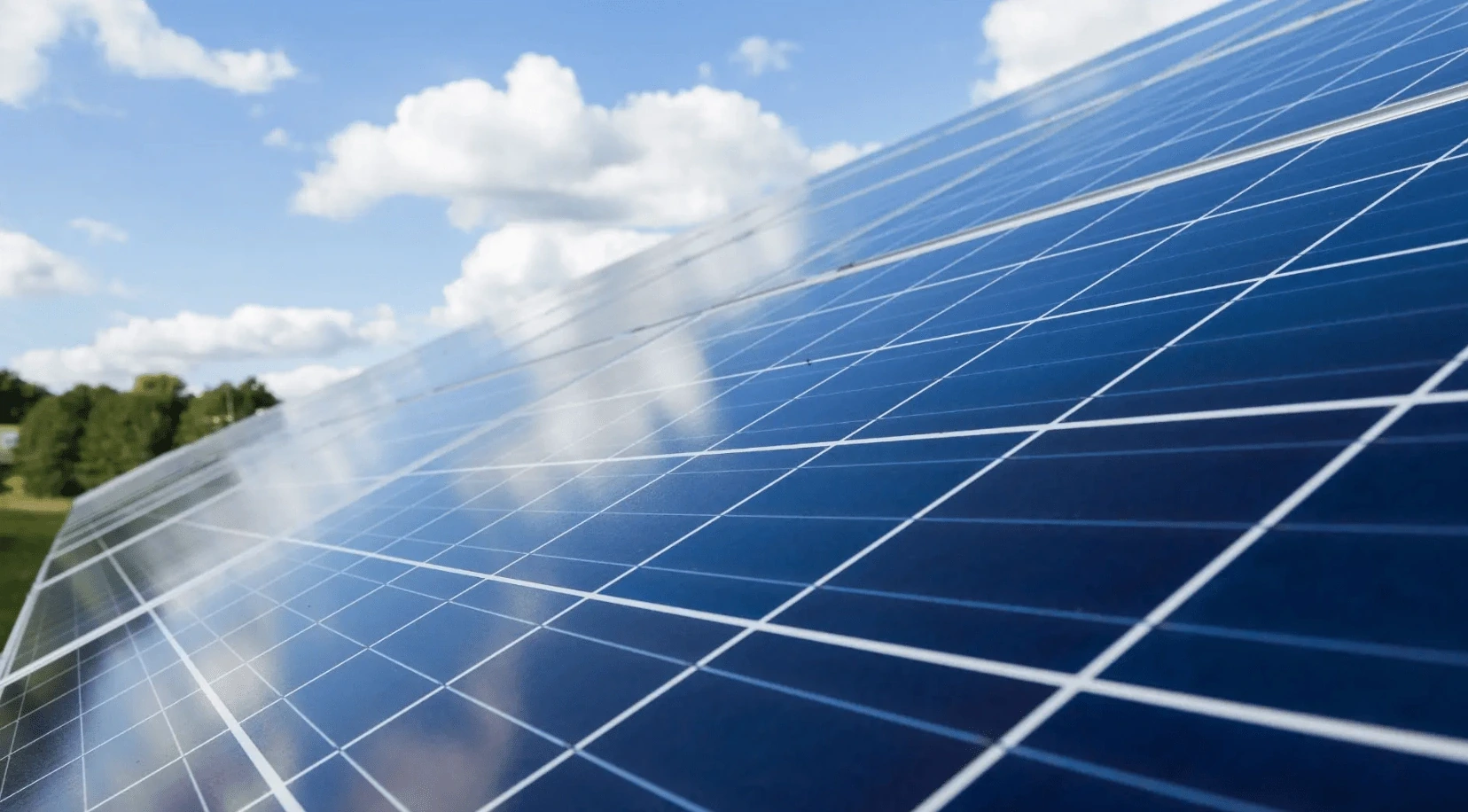 Solar panels under a partly cloudy sky, reflecting sunlight with trees in the background.