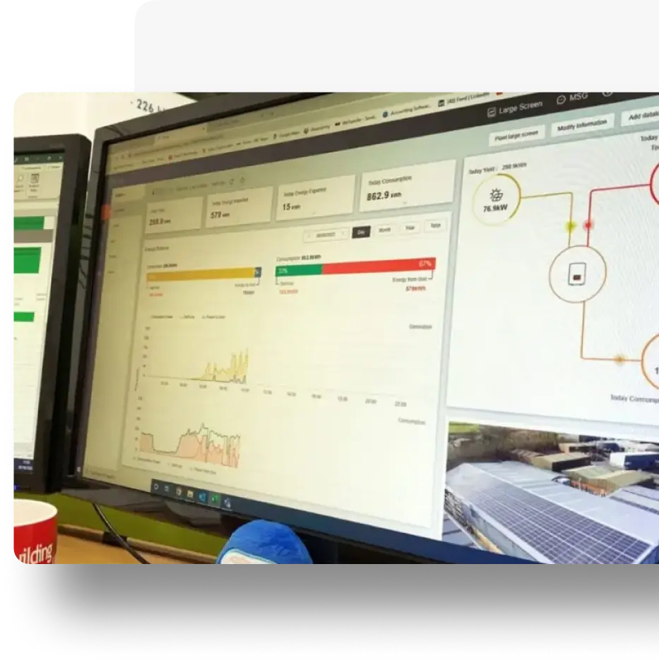 Dual monitors displaying energy and cost dashboards, including graphs and solar-related metrics.