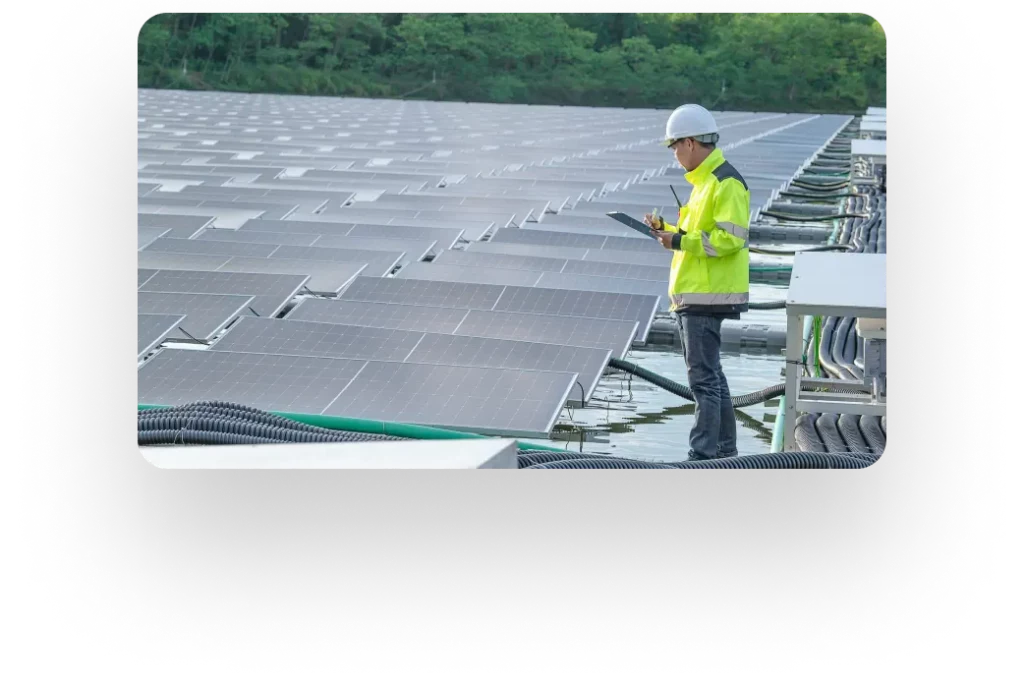 Person in safety gear inspecting solar panels using a tablet outdoors.