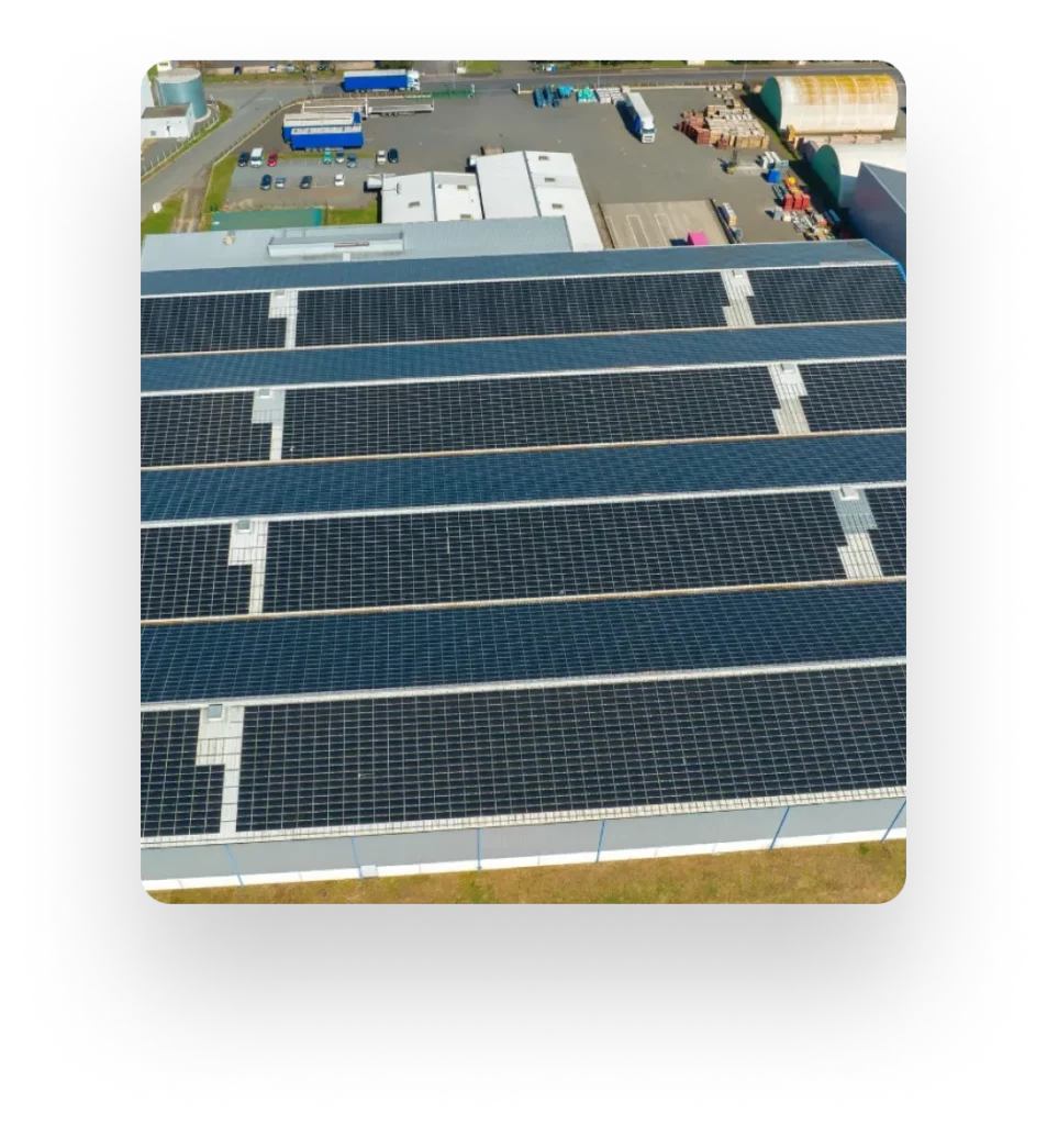 Aerial view of buildings with solar-panel-covered roofs, cars, and industrial materials.