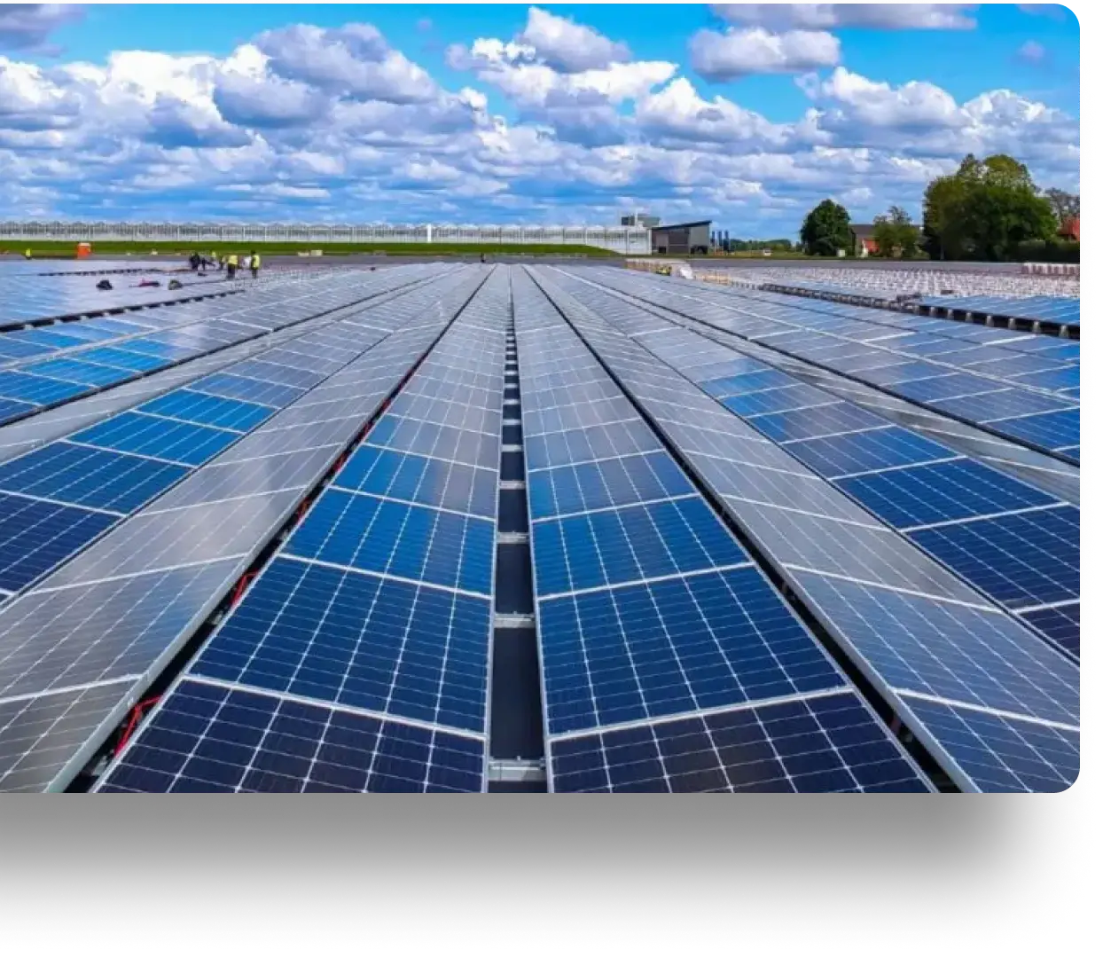 Expansive solar panel array in open field under partly cloudy sky, with buildings in the background.