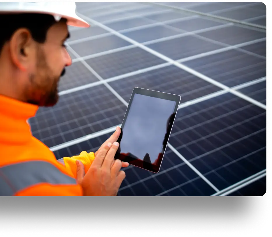 A person in an orange jacket and hard hat uses a tablet while standing in front of solar panels. The focus is on the technology being used for monitoring or managing solar energy systems.