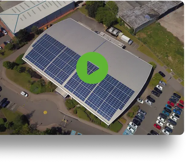 Aerial view of a building with a rooftop solar panel array and adjacent parking lot.