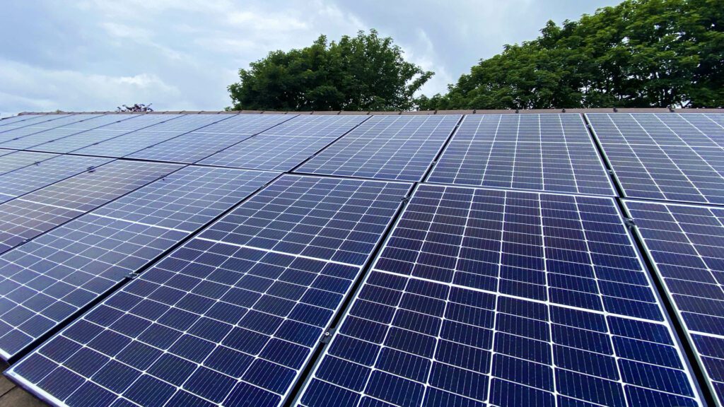 Rooftop solar panel array with cloudy skies and surrounding trees, illustrating renewable energy use.