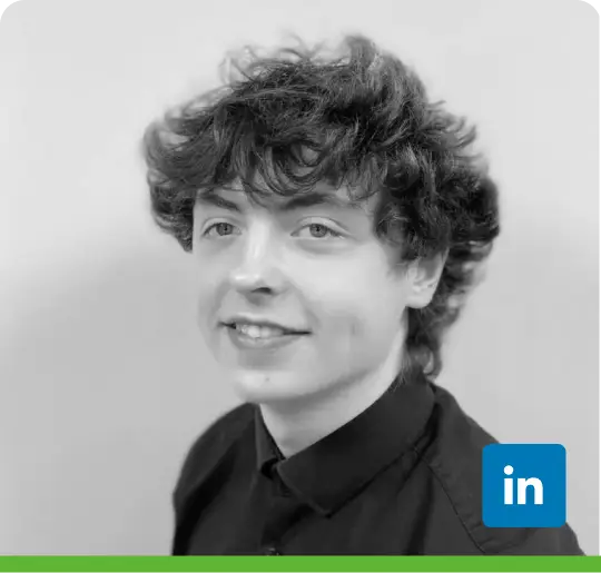 A person with curly hair smiles slightly, wearing a dark collared shirt. The black and white image has a green bar at the bottom, and the background is light-colored.