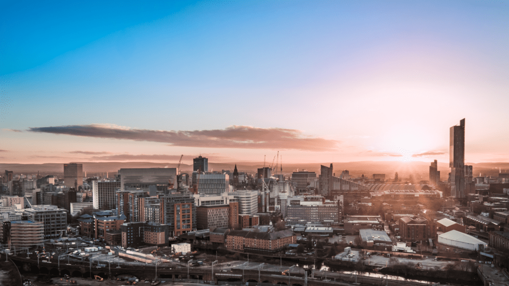 City skyline during sunset, with high-rise buildings, cranes, and a gradient sky transitioning from blue to orange.