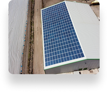 Aerial view of the D&L Growers warehouse with a solar panel-covered roof, surrounded by dirt roads; a large tarp is to the left, highlighting green energy efforts.