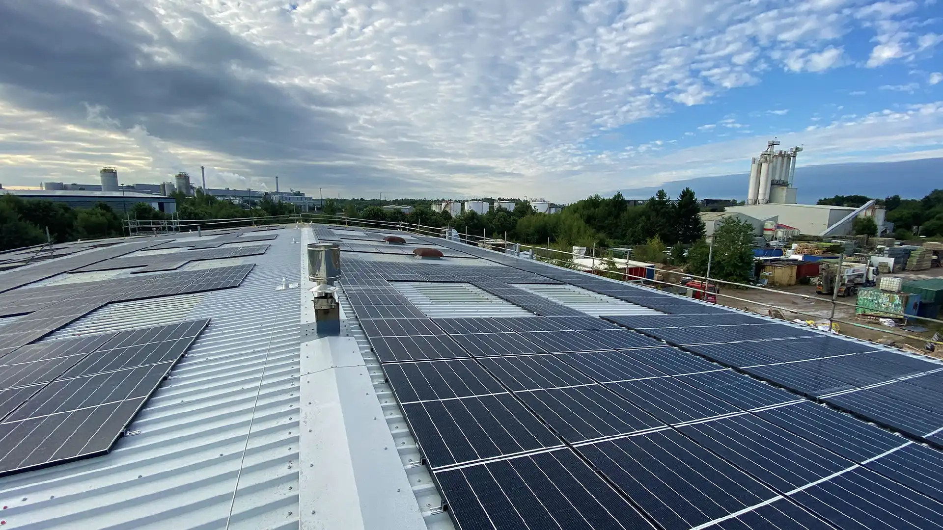 A rooftop with solar panels under a partly cloudy sky, representing the Dean Groups focus on sustainability, with industrial buildings and greenery in the background.