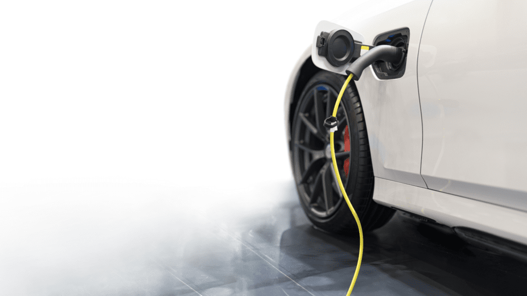 White electric car charging at a station with a yellow cable, parked on a tiled surface amid light mist.