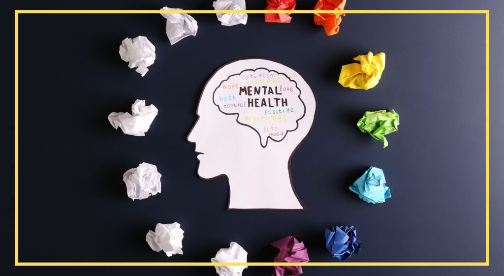 Cut-out silhouette of a head with mental health-related words inside, surrounded by crumpled colored papers.