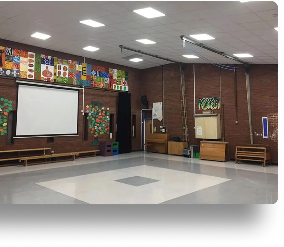 A spacious gymnasium with a polished floor, brick walls, and colorful decorations, including paper trees and artwork.