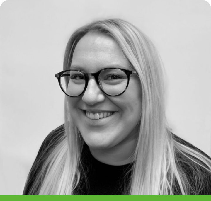 A person with long, light hair and glasses is smiling at the camera, wearing a dark top. The black-and-white image features a rounded green border at the bottom.