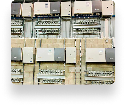 A wall with Instarmac electrical panels and devices in neat rows and columns, featuring switches and control boxes connected by metal conduits on a light brick background.