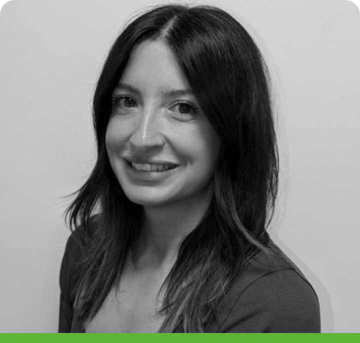 A black and white portrait of a person with long dark hair, smiling slightly, looking at the camera. They are in a casual top against a plain background; a green bar is below.
