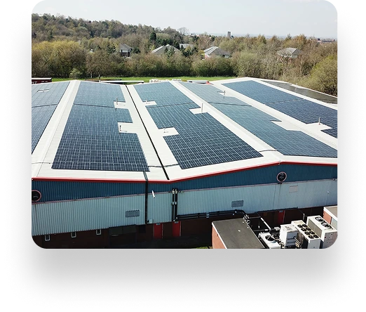 Aerial view of a large industrial building with Quantum Profile Systems solar panels on the roof, surrounded by trees and buildings under a sunny sky.