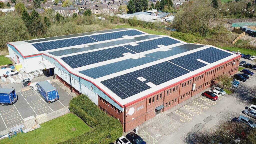 Aerial view of a large industrial building with solar panels on its roof, trucks parked nearby, and 'QPSL' text.