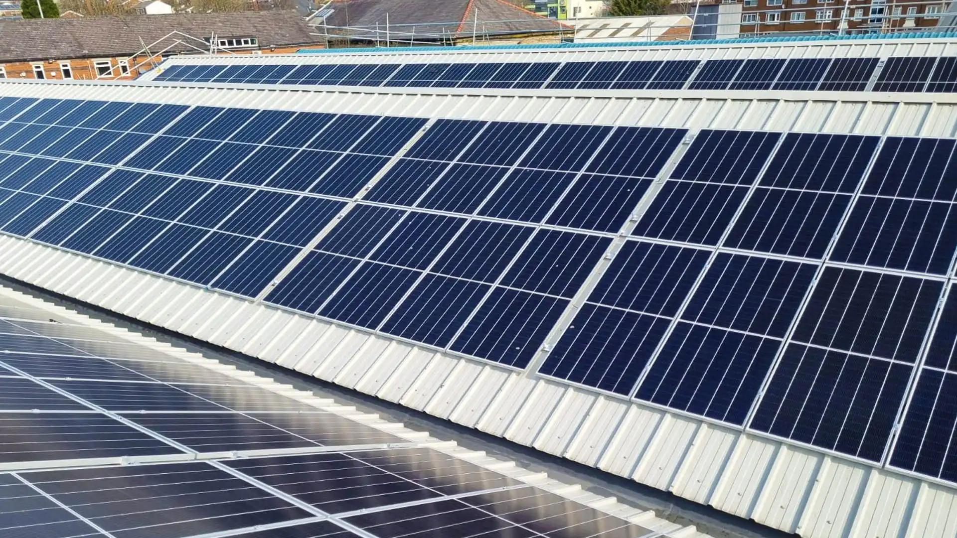 TBE Precision features a rooftop with dark blue solar panels on metal, surrounded by buildings and a clear sky.