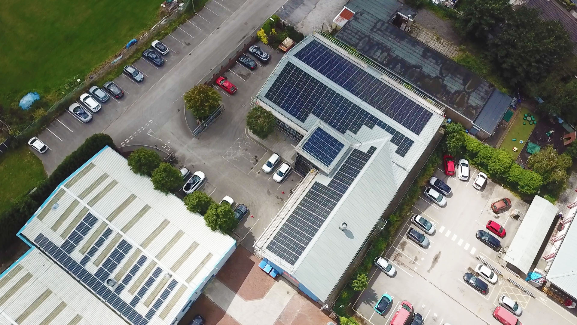Aerial view of buildings with solar panels on rooftops, surrounded by parking lots and green spaces.