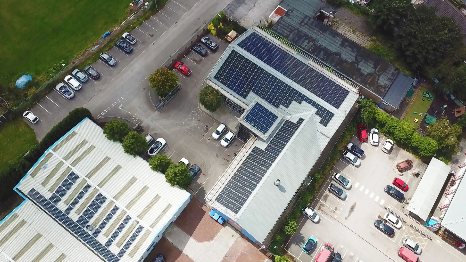 Aerial view of buildings with solar panels on rooftops, surrounded by parking lots and green spaces.