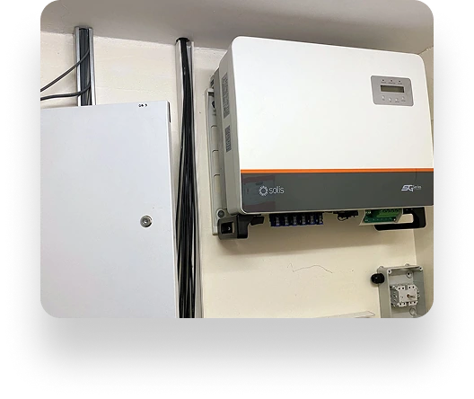 Image of a Solis solar inverter installed on a wall in Alt Valley. Nearby, theres an electrical panel with black cables running vertically. A small white control box is positioned beneath the inverter.