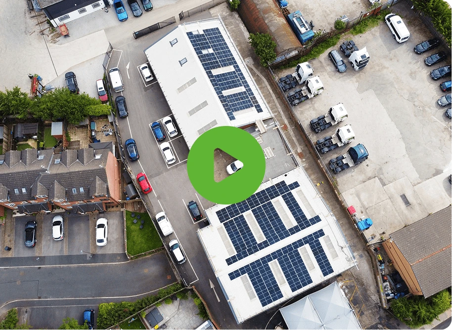 Aerial view of buildings with solar panels framed by Bolton Steel Structures; vehicles are parked around them. Nearby, residential houses and green trees are visible. Green play button overlaid in center.