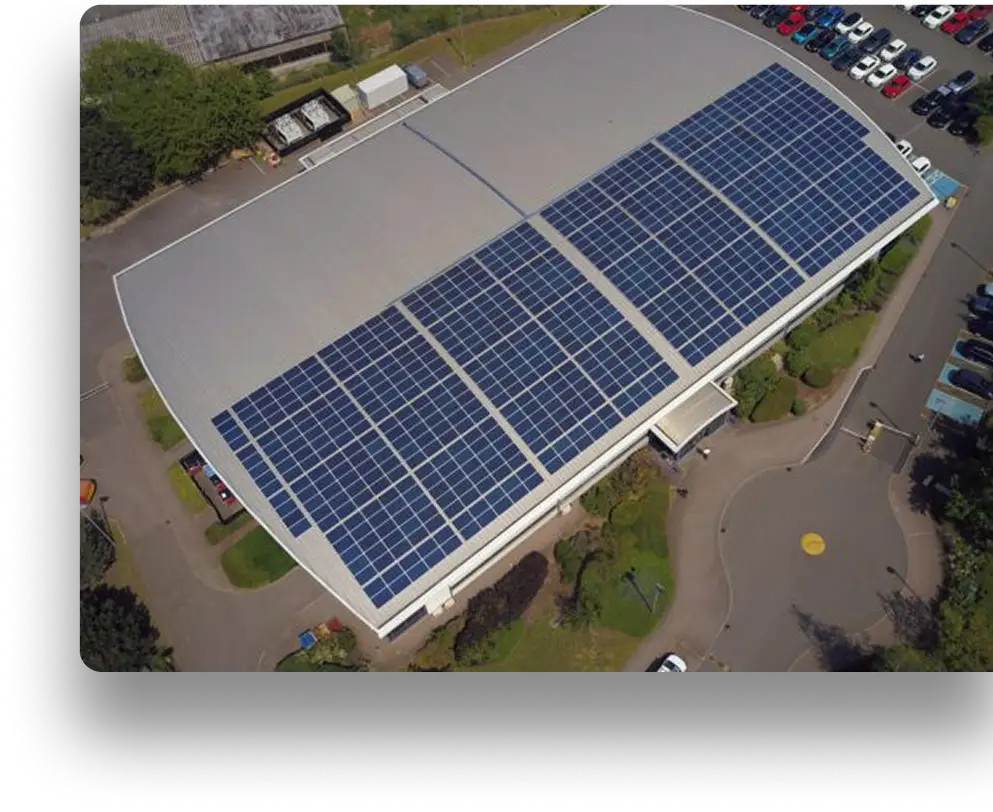 Solar-panel-covered roof of a building amidst parking, trees, and pathways.