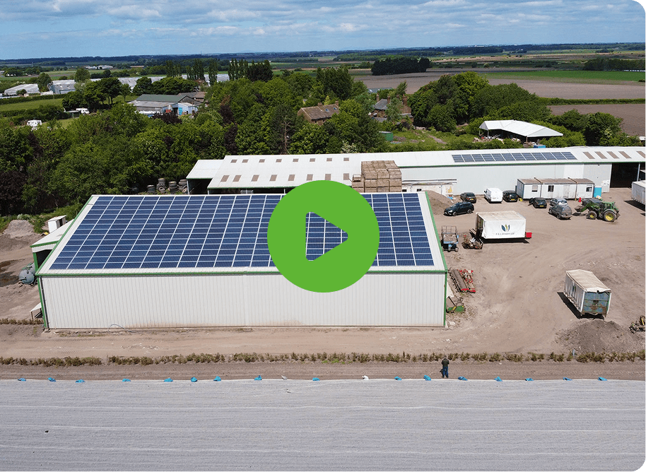 Solar panels covering the roof of a large building, with materials stacked nearby and a play button icon.