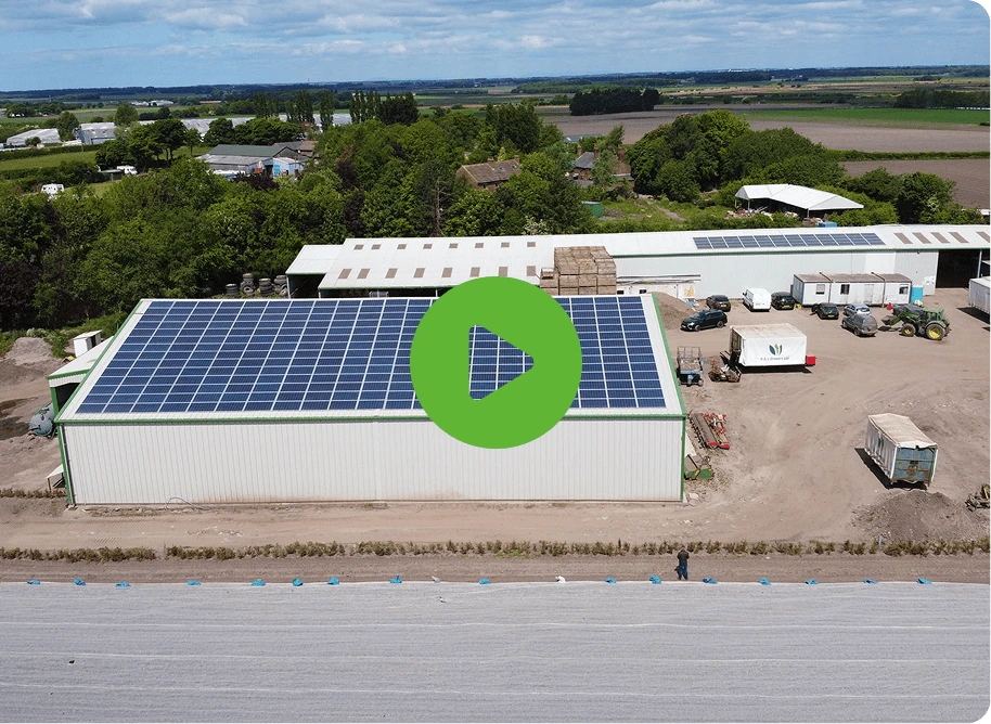 Solar panels covering the roof of a large building, with materials stacked nearby and a play button icon.