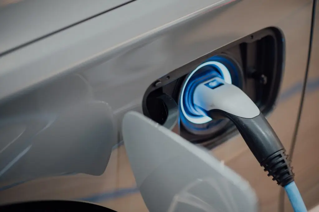Electric vehicle charging with a blue-ringed port, red cable, and a sleek modern design in a parking space.