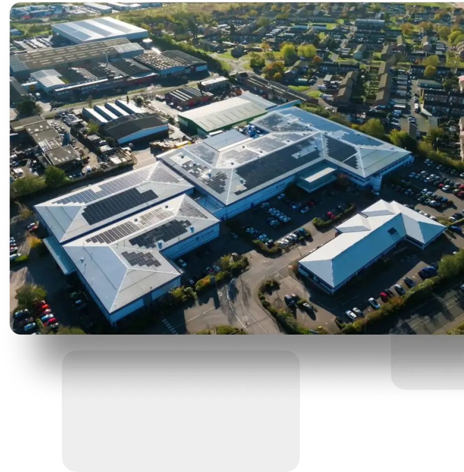 Aerial view of industrial complex with white roofs and solar panels, surrounded by cars.