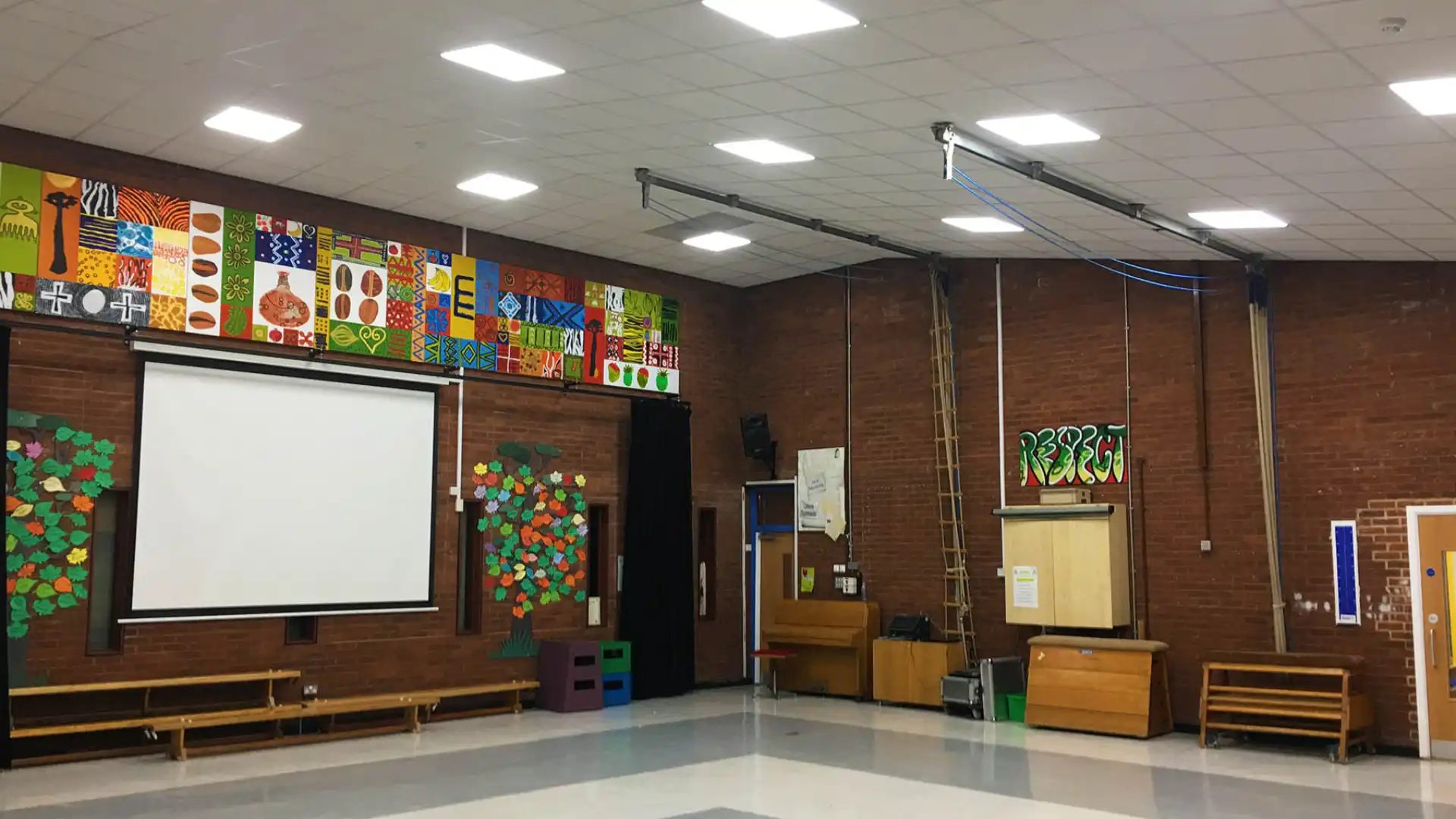 School gymnasium with a high ceiling, lights, gym gear, and a screen.