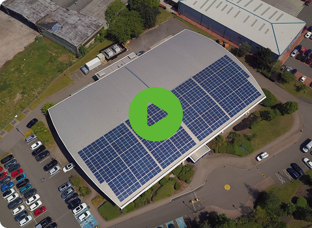 Aerial view of a commercial building with solar panels on its roof, surrounded by parked cars and industrial area.