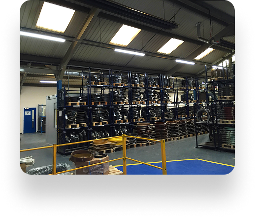 An industrial warehouse interior with high metal shelves full of diverse items. The clear floor, yellow railing, and bright lights highlight the organized space with Kadant equipment enhancing efficiency.