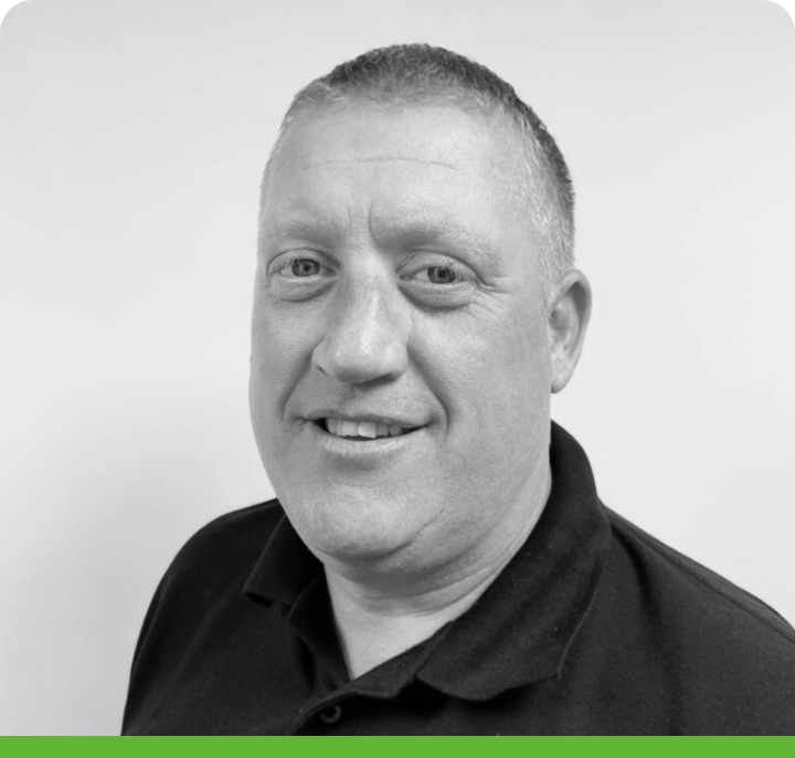 Black and white portrait of a short-haired person in a dark polo shirt. Plain background with a green border at the bottom of the image.