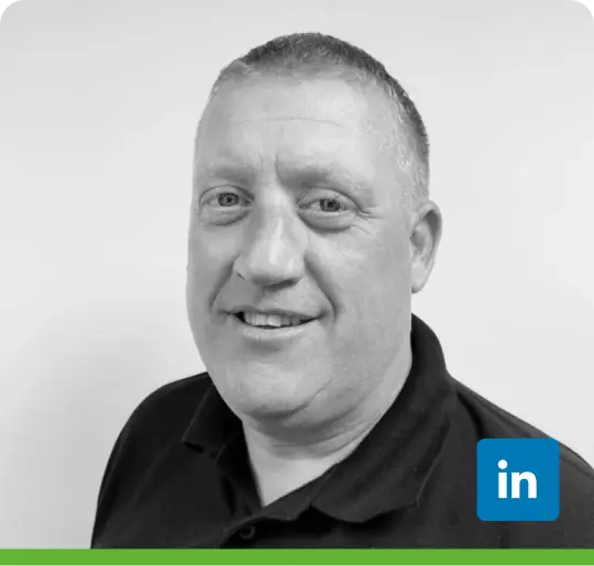 Black and white portrait of a short-haired person in a dark polo shirt. Plain background with a green border at the bottom of the image.